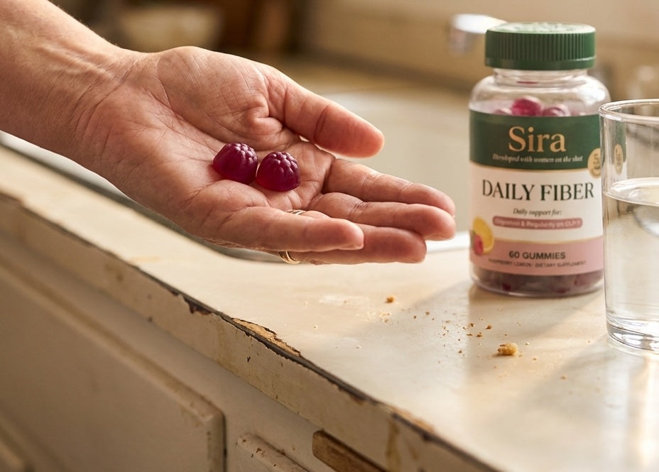Two Sira Daily Fiber gummies in hand with a glass of water